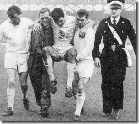 Les Cocker and Johnny Giles carry Willie Bell off at Everton with Jim Storrie looking on in concern